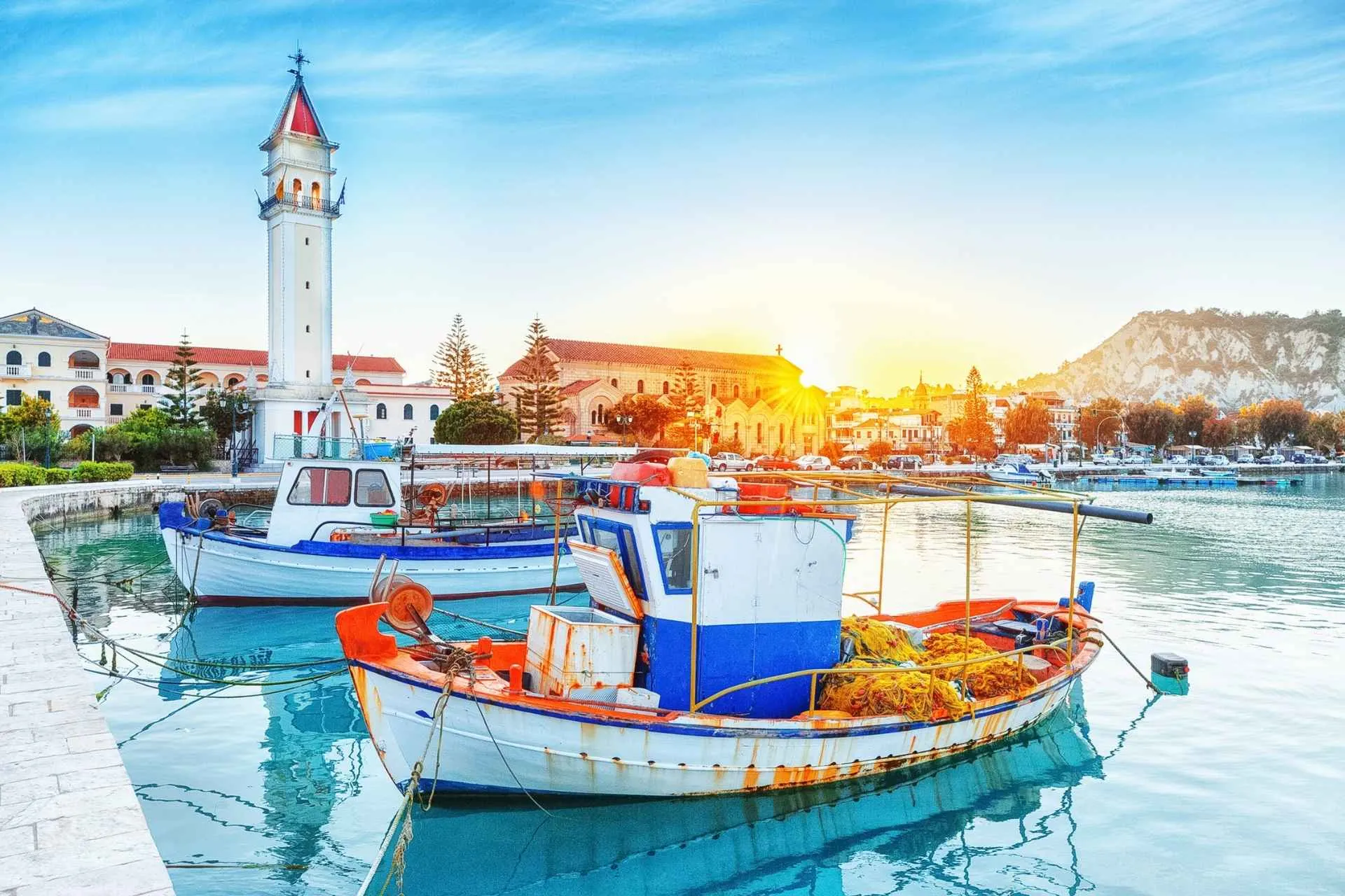 Het eiland Zakynthos, oude haven met aangemeerde boten en de markante kerktoren. Majestueus zonsonderganglandschap, de zon schijnt prachtig met een vakantie Zakynthos met de Jong Intra Vakanties